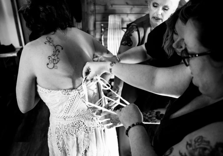 bridesmaids help bride with putting a wedding dress on.
