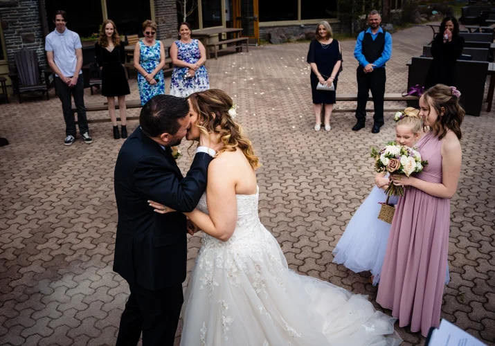 First kiss during elopement ceremony in Banff. Guests happy to see kissing couple.