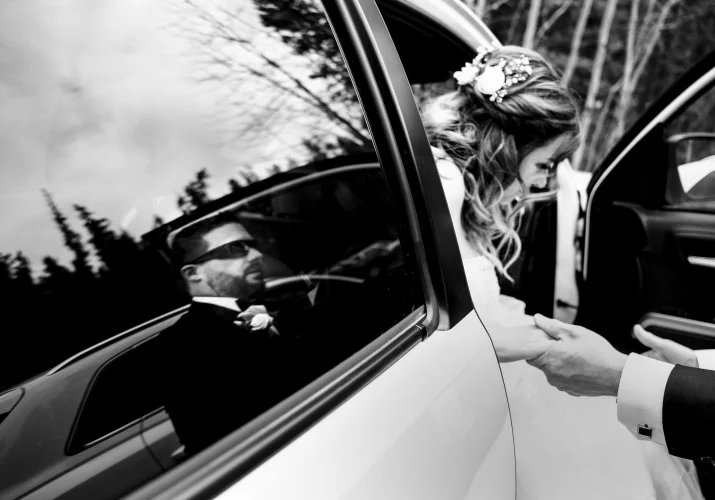 groom's reflection in the car window while he helps the bride go out from the wedding limo.