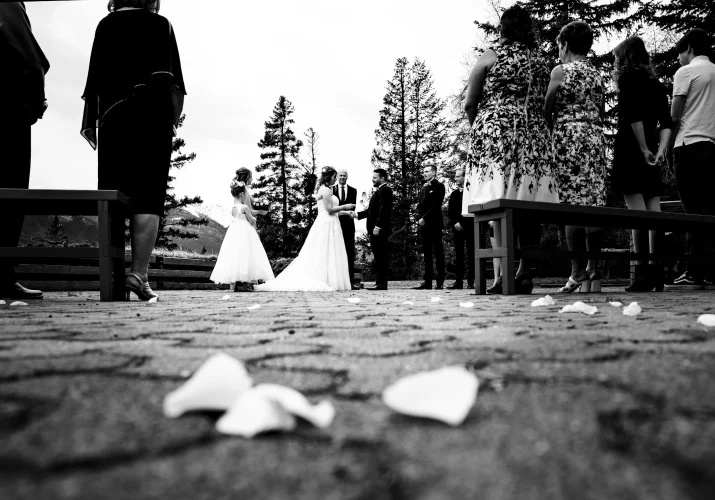 Elopement in black and white. Bride and groom hold their hands. White rose petals on the ground.