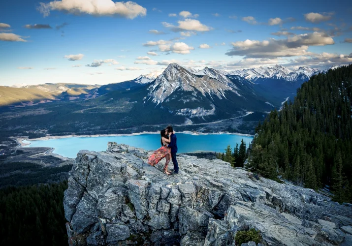 Engaged couple standing on a giant rock. On the background are Canadian Rocky Mountains and turquoise lake.