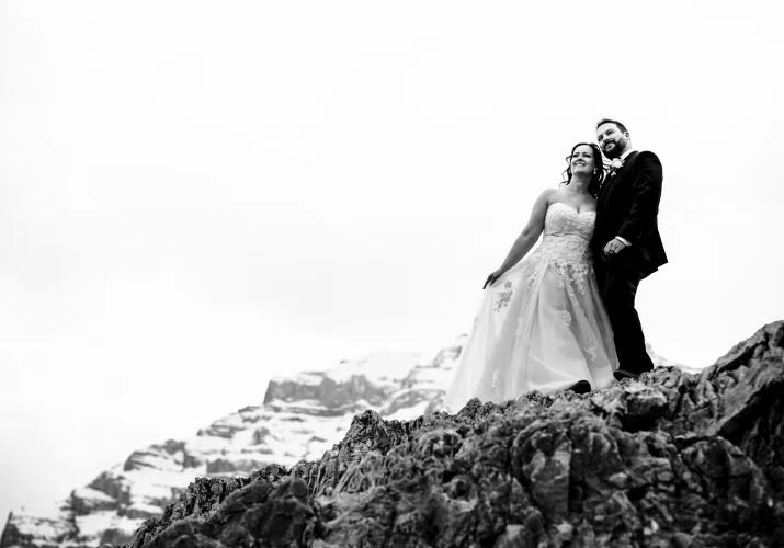 Newlyweds stand at the giant rock in the Canadian Rockies. Black and white photography captured by Calgary Wedding Photographer.
