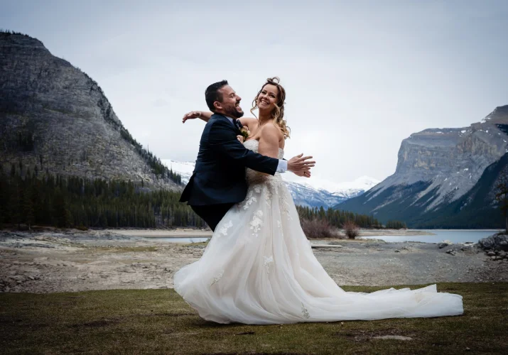 Newlyweds run into each other and hug at Minnewanka Lake in Banff.