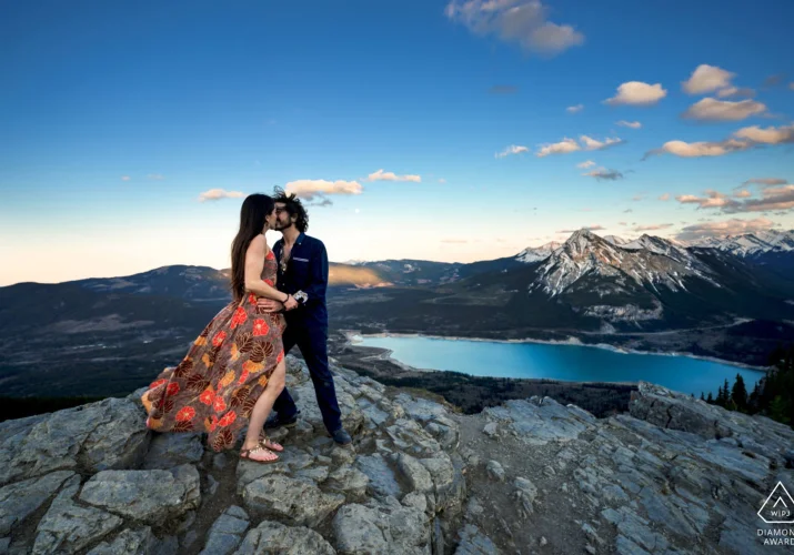 Pre-wedding photo of couple standing on the giant rock against stunning view of blue lake in Kananaskis Country in Canada.