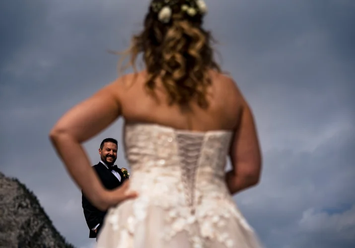 Groom look at the beautiful bride. His reaction captured through the bride's hand. Creative photography by Calgary Wedding Photographer.