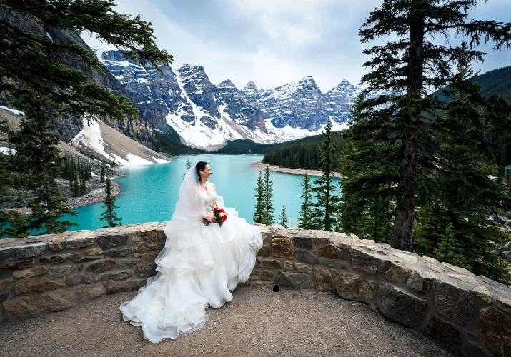 Brides portrait at Moraine Lake. She sits on the dyke against blue lake and Rocky Mountains