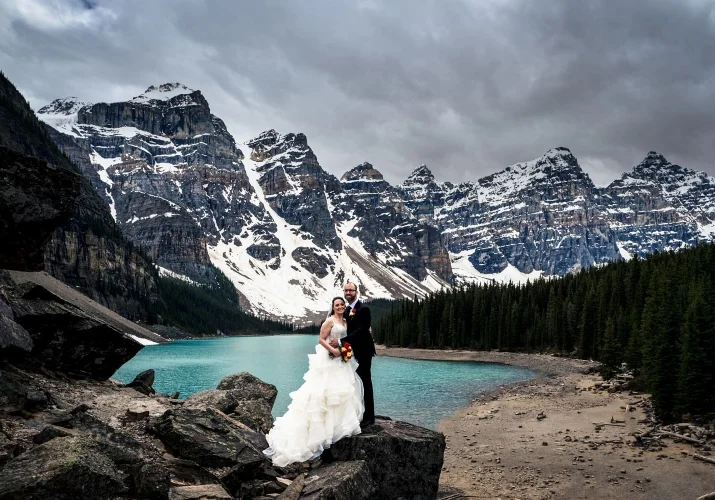 Newlyweds portrait and Moraine Lake. They are surrounded by tremendous Rocky Mountains and blue Lake.