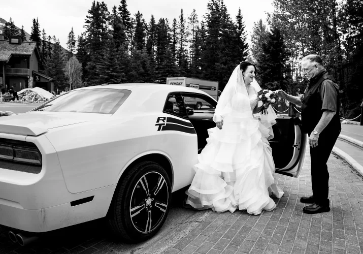 Bride is getting out from a white car to the wedding ceremon in Banff. Her dad helps her.