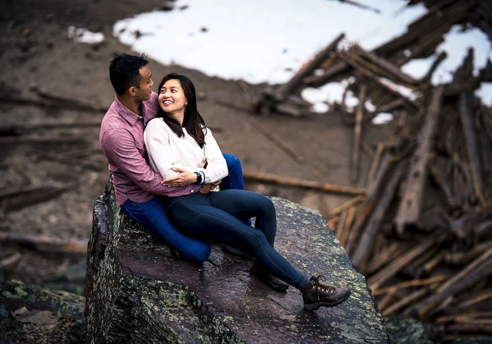 Lovely couple sit on the stone, they smile, hug and look at each others eyes.