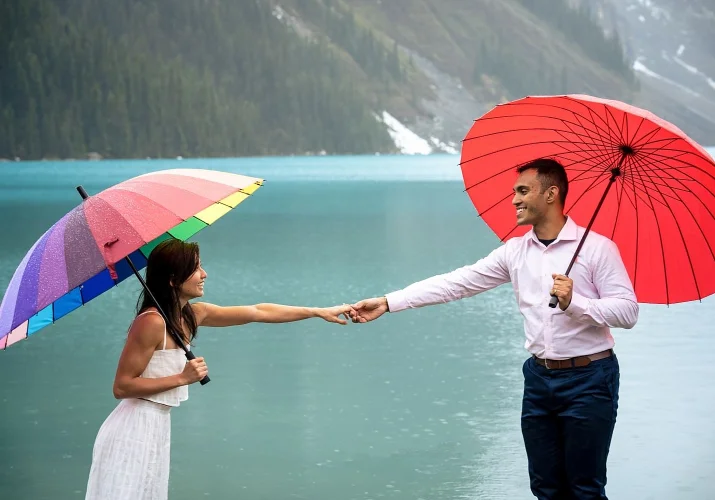 beautiful girl and handsome man hold their hands. They are under umbrellas on the rainy ray at Lake Louise.