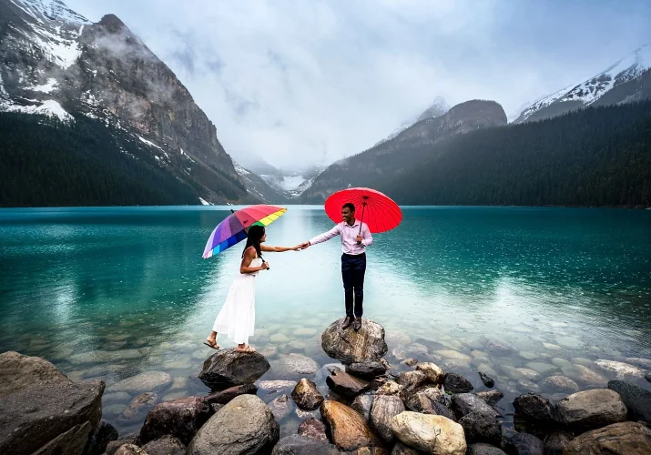 Engaged couple stand at the rocks away from each other trying to reach each other. Engagement at Lake Louise with 4Eyes Photography.