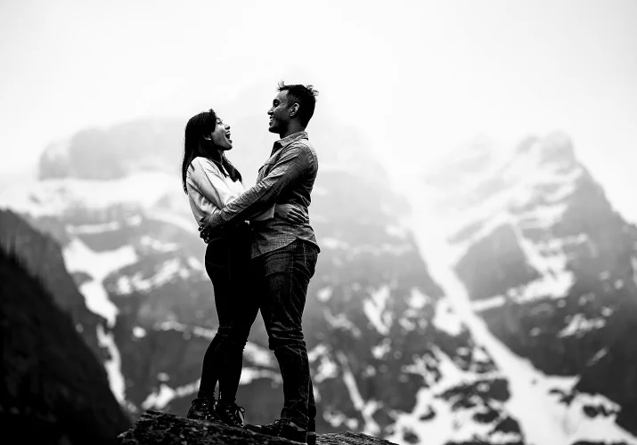 Beautiful engaged couple look at each other and laugh the snowy mountain background.