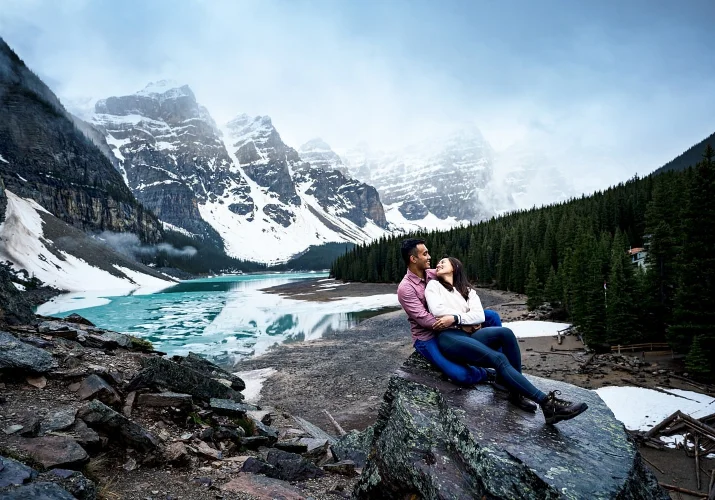 Moraine Lake engagement by the best Banff Wedding Photographer. Couple sitting at the rock over the lake.