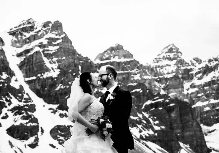Newlyweds kiss. They use noses to kiss. Funny photography n black and white against mountains in Banff.