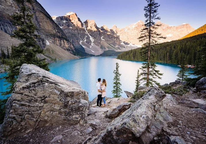 Engagement portrait from Moraine Lake of hugging couple who look at the lake.