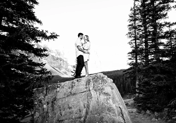 Engagement photography in black and white of couple hugging and standing on the huge stone in Banff National Bark.