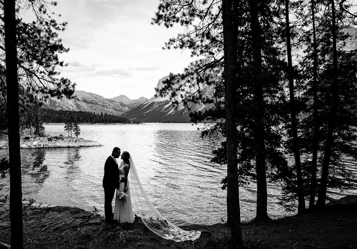 Bride and facing each other an touches their noses. Stunning wedding portrait by the lake in black and white