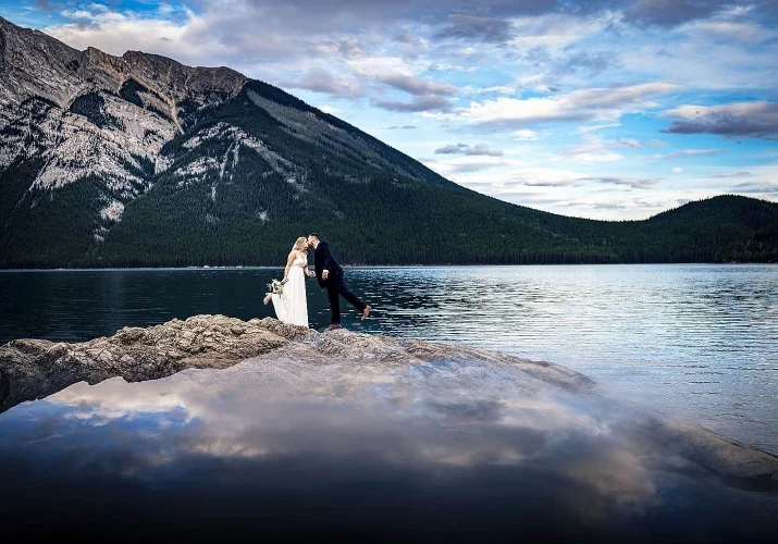 Bride abd grom share a kiss an the huge island by the Minnewanka Lake in Banff