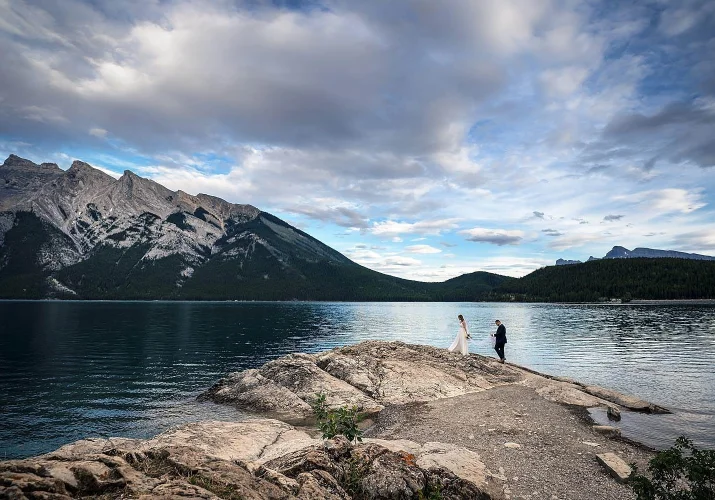 Newlyweds climb the big rock in Banff by the Minnewanka Lake.