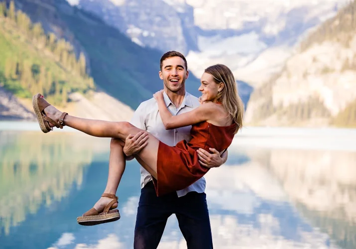 The men is caring his fiancee on his hands during fun Banff Engagement at Lake Louise.