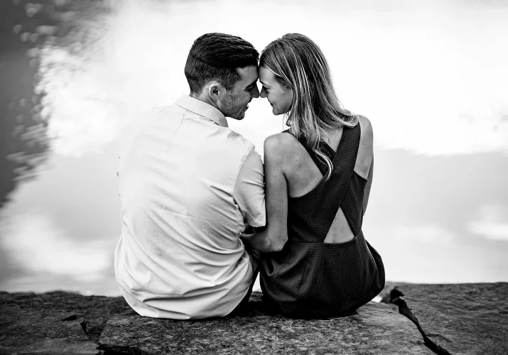 Cute photograph of engaged couple sitting by the lake ,