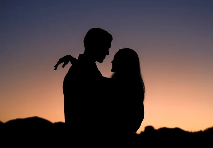 A Canadian, Banff Wedding and Engagement Photographer created creative, situate photograph of engaged couple back-lit by the sunrise at Moraine Lake