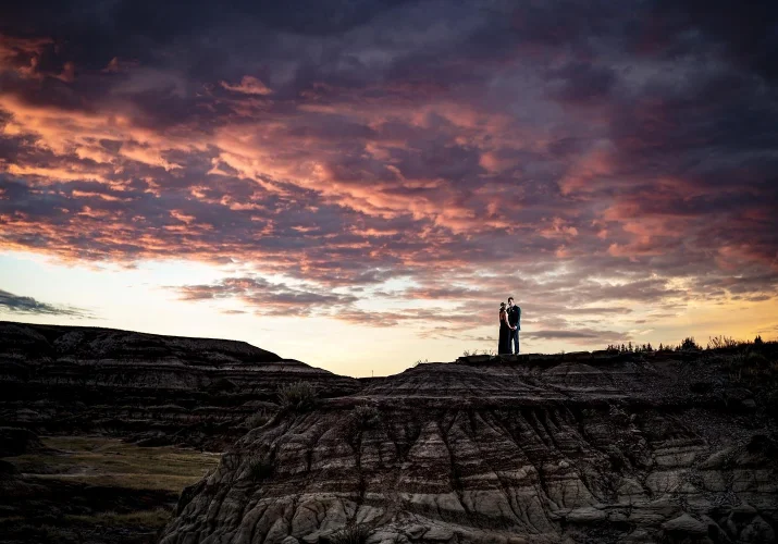 Tiny people in love hugging each other on the top of Horseshoe Canyon in Dramheller. Behind them amazing and colourful sunrise.