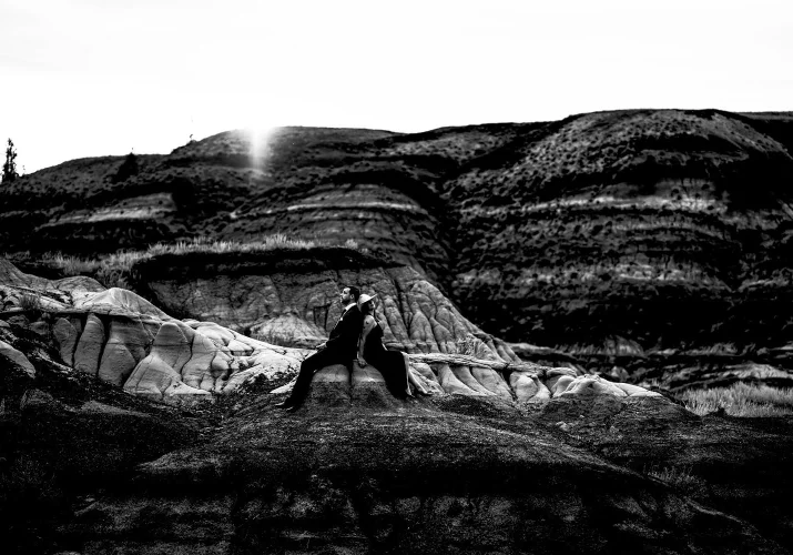 Engaged couple sits back to back . On the background powerful Horseshoe Canyon in Alberta.