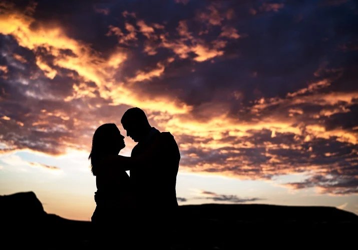 Silhouetted engaged couple against colourful sunrise