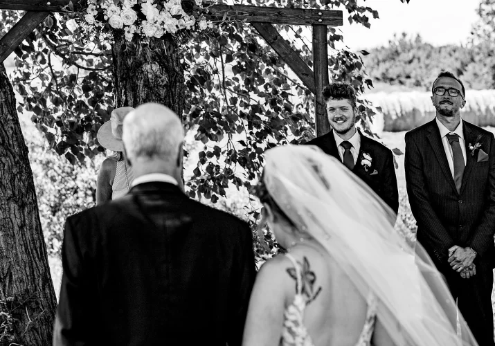 Father walks the bride down the aisle. The groom look at the bride and smiles.