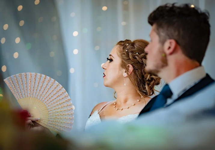 Bride and groom on the reception. Bride cools herself down with a hand fan.
