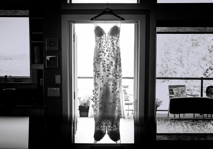 Amazing black and white photograph of a wedding dress hanging on the window frame.
