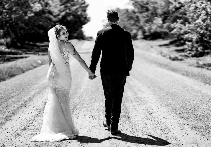 Bride and groom walk on the dirt road in Calgary. Bride looks at the camera.