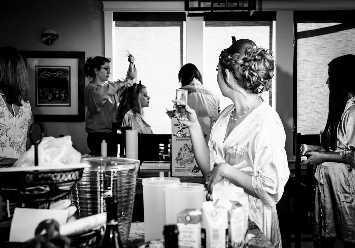 Black and white photograph during Calgary wedding. Bridesmaid having a hair done and the bride look at her with a glass of champagne in her hand.