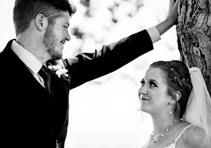 bride lean over a tree and the groom put his hand on the tree looking deeply into bride's eyes