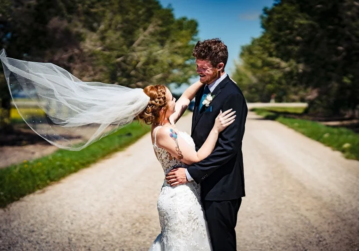 Bride and room in a hug, looking at each other. Bride's veil fly with the wind.