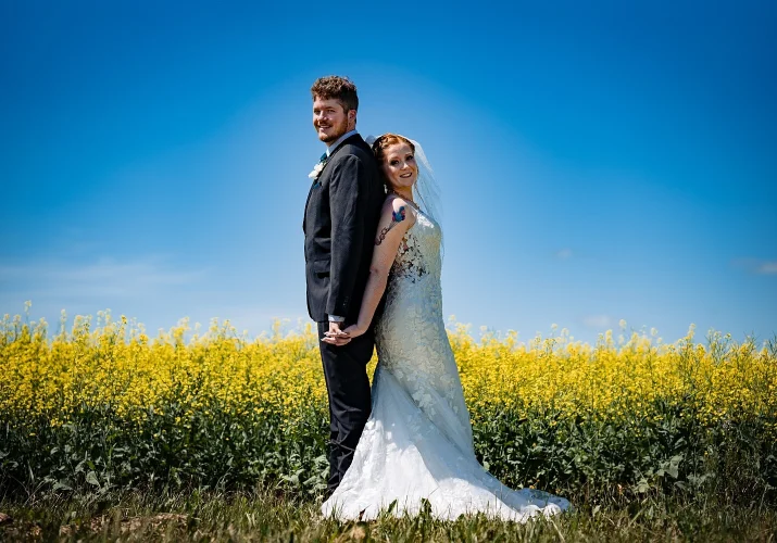 Newlyweds stand back to back and hold hands in canola filed in Calgary.