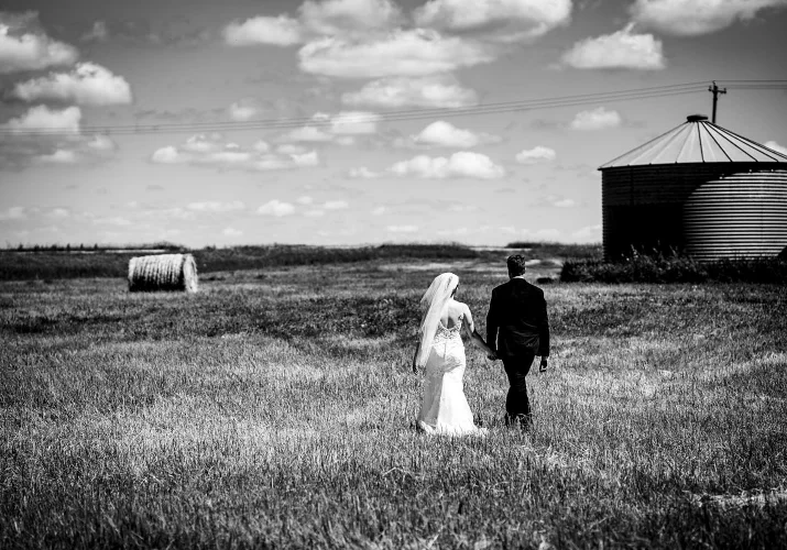 Black and white wedding photograph of newlyweds walking on the filed outside Calgary.