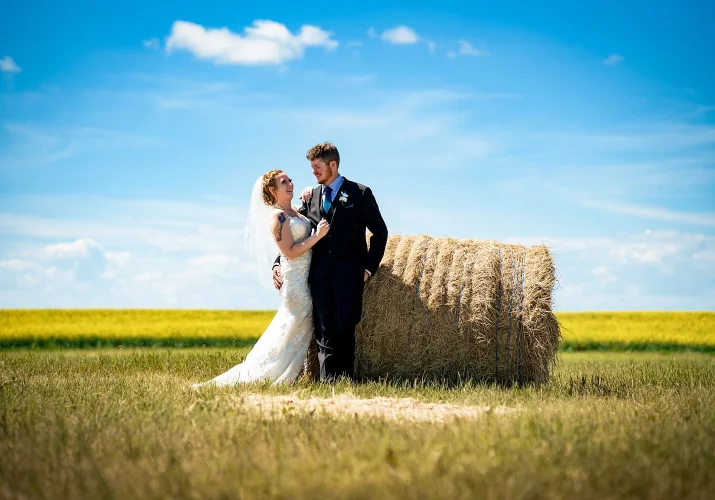 Groom lean against hay cone and the bride is next to him looking deeply into his eyes.