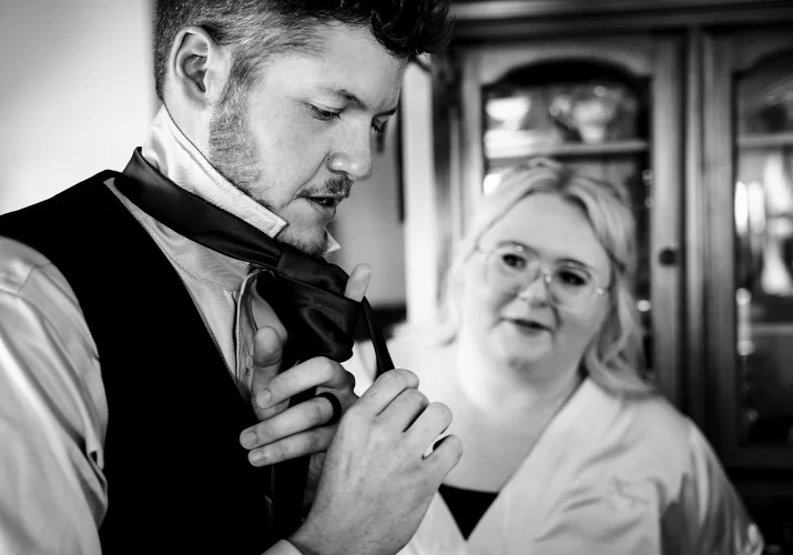 Groom tries to tie his tie. His friend look at him.