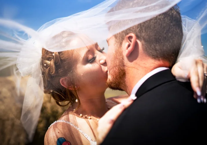 Bride and groom share a kiss under a veil.