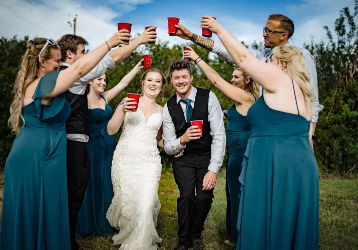 Bridal party creates a tunnel with their hands and drinks in their hands. Bride and groom walks through that tunnel.