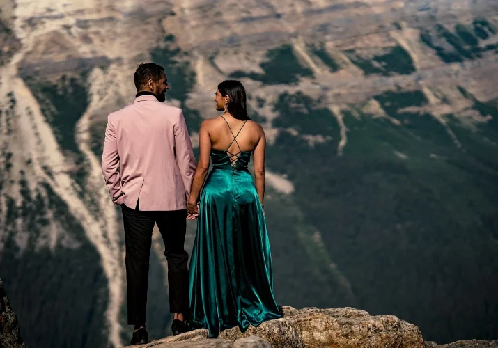 A man in a suite and a lady in a long, green dress from behind. They look at each other.