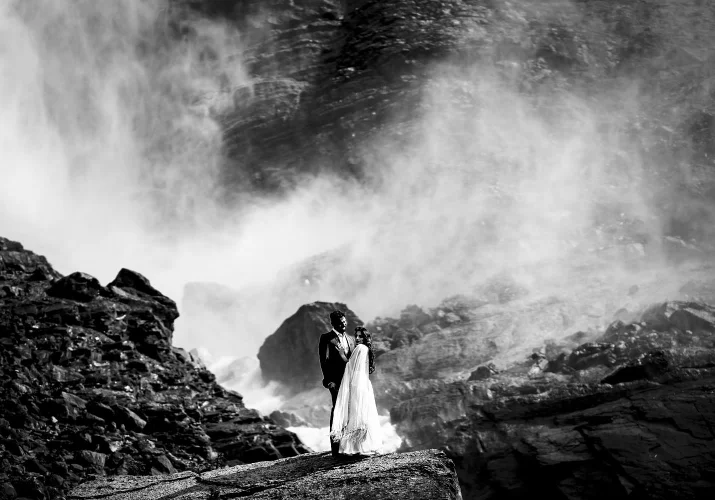 Engagement photo session at Takakkaw Falls in Canada with Indian couple. They are dressed in traditional outfits and hug each other.j