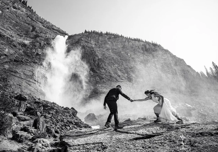 Man helps his fiance to fight strong wind at Takakkaw Falls.