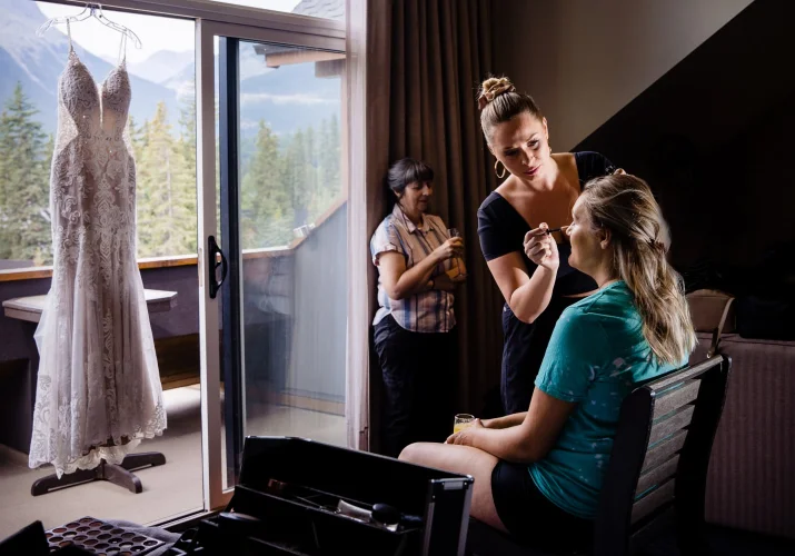Wedding dress hanging at the window while the bride is getting her make up done.