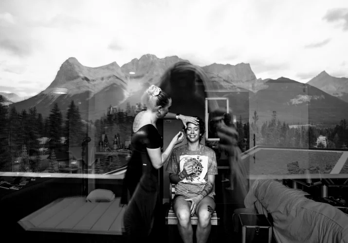 Black and white photograph of the bride getting her make up done . In the window amazing reflection of the Cnadian Rocky Mountains