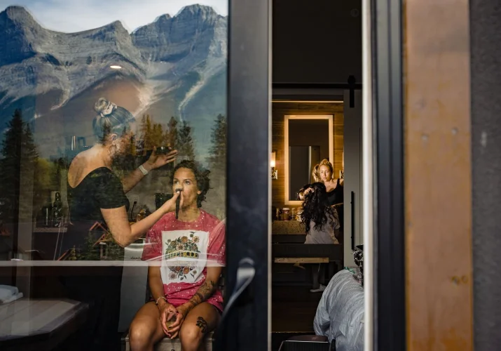 unique photograph of getting ready time before Banff Wedding . Bride and bridesmaid getting their hair and make up done. Photography through the window.