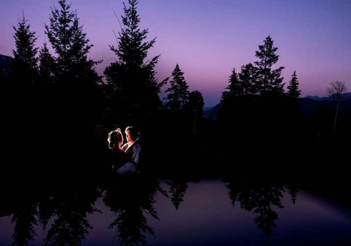 Creative photograph of back-lighted bride and groom in the dark forest with reflection of the trees.