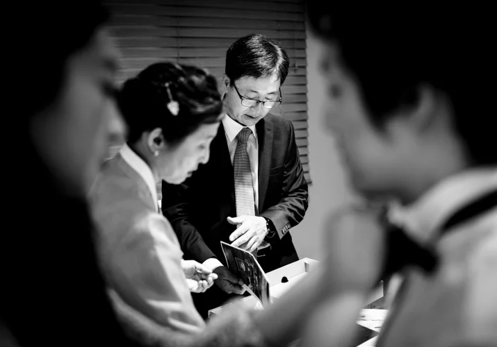 Getting ready time in black and white . Sister of the groom helps with his bow tie while parents look at the old photos.